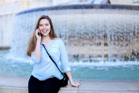 Young woman talking by smartphone in Trevi fountain background. Concept of modern technology, advantageous tariff plan and summer vacations in Europe.の写真素材