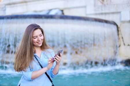 Young caucasian girl chatting by smartphone in Trevi fountain background. Concept of modern technology, advantageous tariff plan and summer vacations in Europe.の写真素材