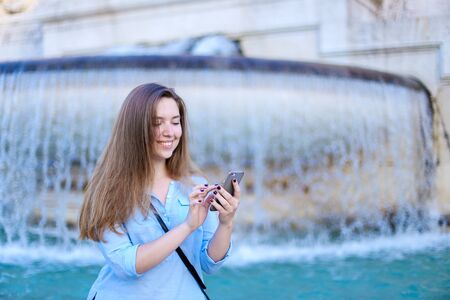 Young businesswoman chatting by smartphone in Trevi fountain background. Concept of modern technology, advantageous tariff plan and summer vacations in Europe.の写真素材
