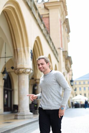 Young caucasian man walking on square near building with columns, wearing grey sweater. Concept of visiting Europe and tourist.の写真素材