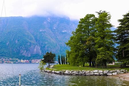 Green trees near lake Como in Mandello del Lario and Alps mountain in clouds. Concept of seascape and park.の写真素材