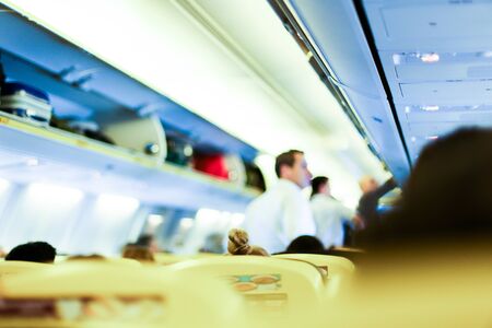 Blurred photo of airplane interior, stewards and passengers with bags on shelves. Concept of cheap tickets and low cost flights.の写真素材