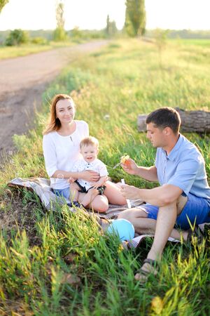 Young american mother and father sittling on grass with little baby and blowing bubbles. Concept of picnic and children, parenthood and leisure time.の写真素材