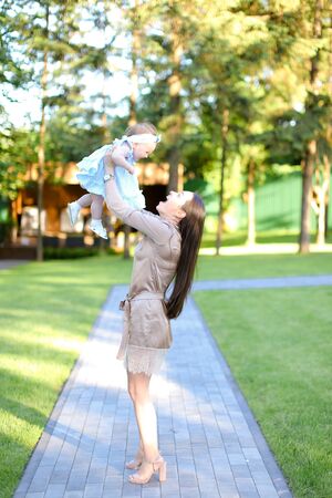 Young happy mother wearing dress holding little baby in garden. Concept of motherhood and resting on open air in park.の写真素材