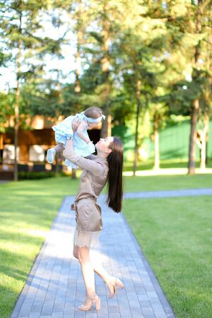 Young caucasian mother wearing dress holding little baby in garden. Concept of motherhood and resting on open air in park.の写真素材