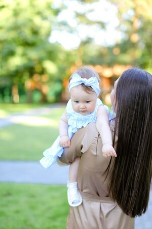 Back view of brunette young mother holding little daughter in garden. Concept of motherhood and resting on open air.の写真素材