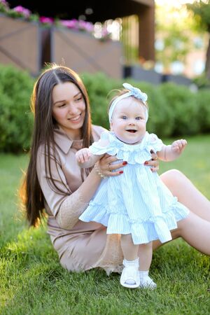 Young woman sitting on grass with little female baby. Concept of motherhood and children, resting on open air.の写真素材