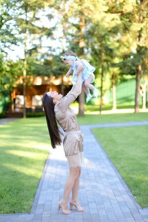 Young european mother wearing dress holding little baby in garden. Concept of motherhood and resting on open air in park.の写真素材