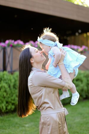Young mother holding and kissing little daughter in grass background. Concept of motherhood and child.の写真素材
