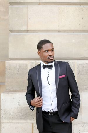 Afro american happy successful man wearing dark suit and standing outside in wall background. Concept of black businessman.の写真素材