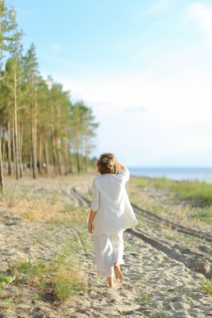 Back view of girl walking on sand beach and wearing white clothes. Concept of summer vacations.の写真素材