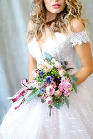 Young bride wearing white dress with bouquet at photo studio. Concept of bridal photo session, wedding and floristic art.の写真素材