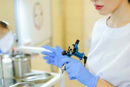 Close up cosmetlogist hands in blue latex gloves keeping microblading machine at beauty salon. Concept of permanent makeup artist and cosmetology equipment.の写真素材