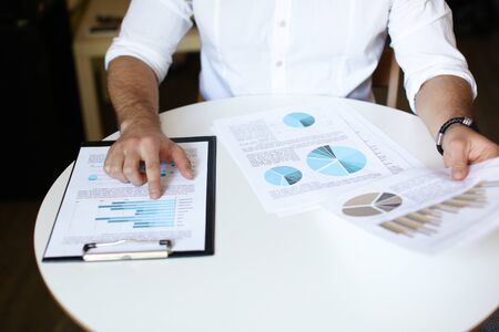 Male caucasian person working with documents and diagrams, wearing white shirt and watch.の写真素材