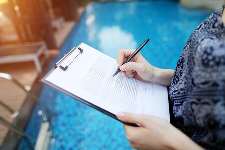 Photographed close hand of girl signing sunny day paper on pool background. concept of signing contract, travel, new contract or arrangement. Front used with Open Font Licenseの写真素材