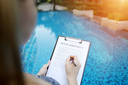 close portrait of signing rental agreement document on background of swimming pool. woman taking apartment for long term. Front used with Open Font Licenseの写真素材