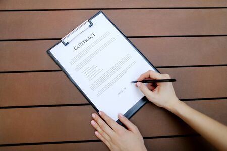 beautiful flat lay of young woman hands with pen sign contract, wooden backgroung. concept of business work agreement, freelance working remotely. Front used with Open Font Licenseの写真素材