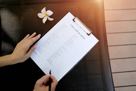 sunlight portrait of woman fill visa application in travel agency. close up hands, pen and document. concept of private retailer or public service provides tourism related services on behalf of suppliers activities, airlines, car rentals, cruise lines, hotels, railways, travel insurance and package tours. Front used with Open Font Licenseの写真素材