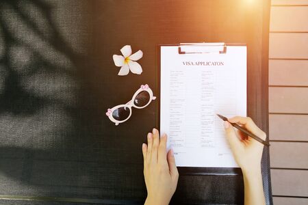 bright flat lay of woman hands fill visa application with pen for travel, sunlight portrait with sunglasses and flower. concept of traveling journey. Front used with Open Font Licenseの写真素材