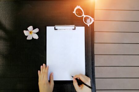 close up sunny portrait of woman hands hold pen and empty paper on holiday sunlight background with flower and sunshine. concept of signing documents, visa application travel. Front used with Open Font Licenseの写真素材