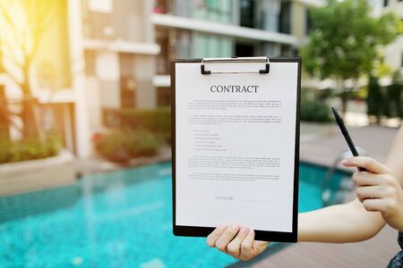 woman is holding pen and contract, proposes to sign document against background of building with apartments. concept of signing papers, travel rental housing. Front used with Open Font Licenseの写真素材