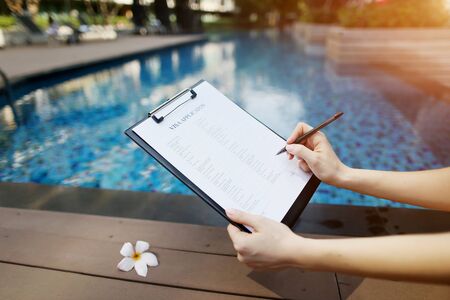 female hand holds out pen, fills out visa application form in United States. Sunny portrait on pool background And sunlight. concept of traveling to new countries. Front used with Open Font Licenseの写真素材
