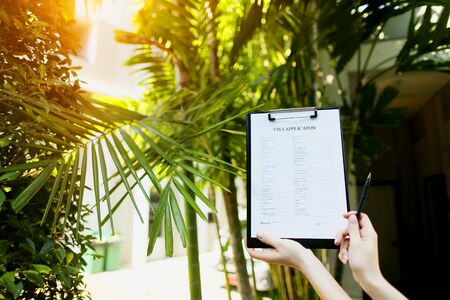 Focus on document, girl fills out visa application form against background of palms and sun and is going to travel to Australia. concept of assistance agencies in preparation of documents, agreements between people or provision of tourist services. Front used with Open Font Licenseの写真素材