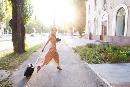Young jocund journalist wearing dress standing outside with camera valise. Concept of photographer profession and summer season, tourism.の写真素材