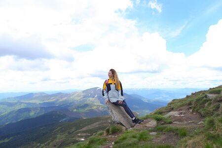 Young pretty female tourist wearing yellow jacket standing in mountains. Concept of spending summer vacations in Alps, tourism and traveling.の写真素材