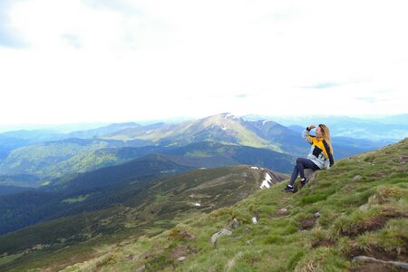 Young relaxed female tourist wearing yellow jacket sitting in Appenine mountains. Concept of spending summer vacations in Alps, tourism and traveling.の写真素材