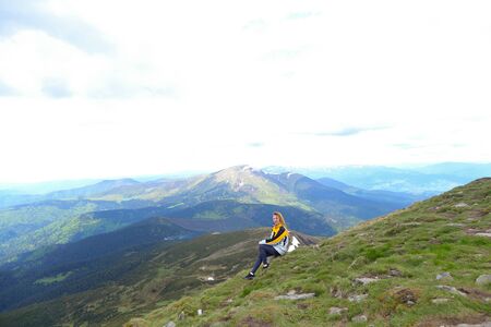 Young female tourist wearing yellow jacket sitting in Appenine mountains. Concept of spending summer vacations in Alps, tourism and traveling.の写真素材