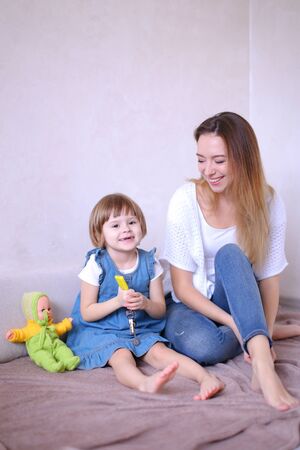 Young mother playing with little daughter and sitting on bed with toy. Concept of children, motherhood and leisure.の写真素材
