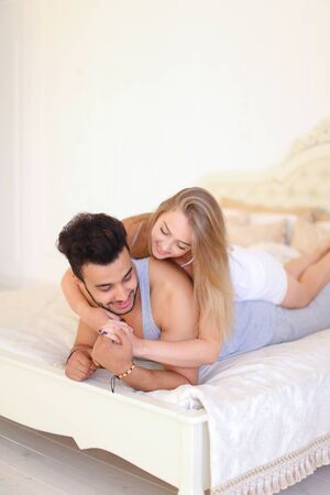 Blonde caucasian girl and hispanic biy lying in bad in morning. Concept of happy couple and resting on weekends in bedroom.の写真素材