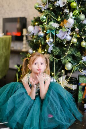 Little nice girl wearing blue dress standing near Christmas tree. Concept of celebrating New Year, fashion and childhood.の写真素材
