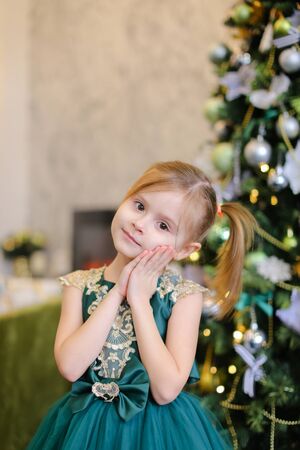 Little caucasian girl wearing blue dress standing near Christmas tree. Concept of celebrating New Year, fashion and childhood.の写真素材