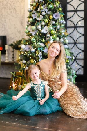 Young mother and little daughter with bengal light sitting on floor near Christmas tree. Concept of celebrating New Year, winter holidays and fashion.の写真素材