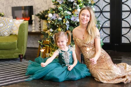 Young mother and little daughter with bengal light sitting on floor near Christmas tree. Concept of celebrating New Year, winter holidays and fashion.の写真素材
