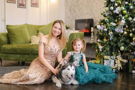 Young mother with little daughter and malamute lying near near Christmas tree. Concept of celebrating New Year, pets and fashionable look.の写真素材