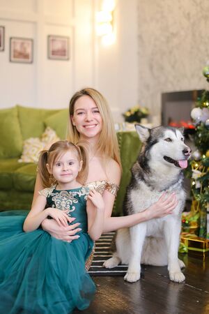 Young gorgeous mother with litle daughter and husky sitting near near Christmas tree. Concept of celebrating New Year, pets and fashionable look.の写真素材