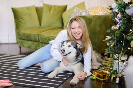 Young caucasian girl lying on floor with malamute near Christmas tree. Concept of pets, celebration winter holidays and New Year.の写真素材