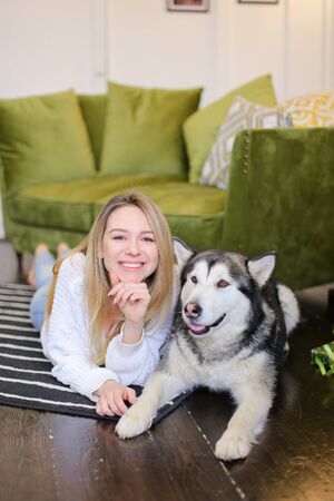 Woman lying on floor with malamute near sofa. Concept of pets and spending free time at home.の写真素材