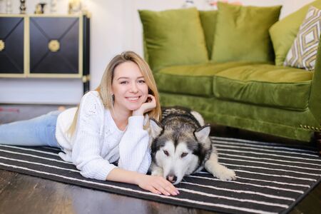 Young woman lying on floor with malamute near sofa. Concept of pets and spending free time at home.の写真素材