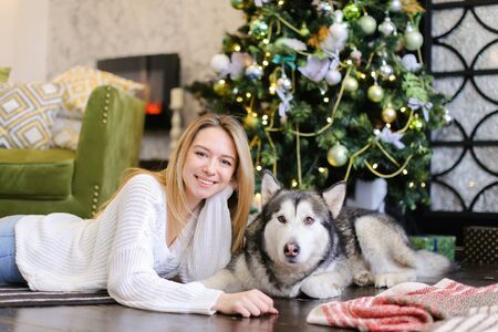 Young smiling girl lying on floor with adult malamute near Christmas tree. Concept of celebrating New Year, winter vations and pets.の写真素材