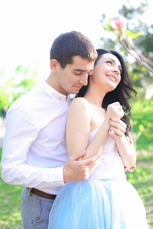 Brunette man wearing shirt, hugging and kissing caucasian girl in park. Concept ofrelationship and feeling, love and spring season.の写真素材