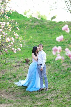 Young caucasian woman wearing blue dress and walking near magnolia with boyfriend. Concept of love and spring season.の写真素材