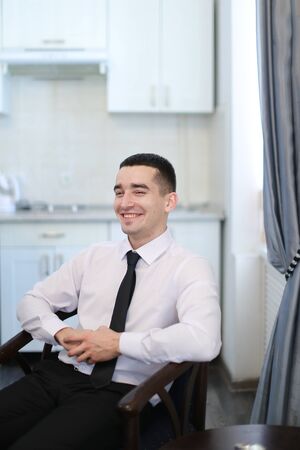 Young businessman wearing white shirt with black tie sitting in chair. Concept of business wear style and successful man.の写真素材