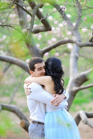 Young lady and brunette man hugging near blooming tree. Concept of love and sping season.の写真素材