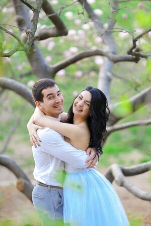 Young nice feale person and brunette man hugging near blooming tree. Concept of love and sping season.の写真素材
