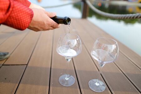 Male hands in red shirt pouring wine on wooden table.の写真素材