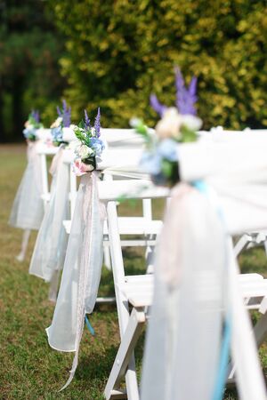 White decorated chairs for wedding in park. Concept of bridal seating for ceremony.の写真素材